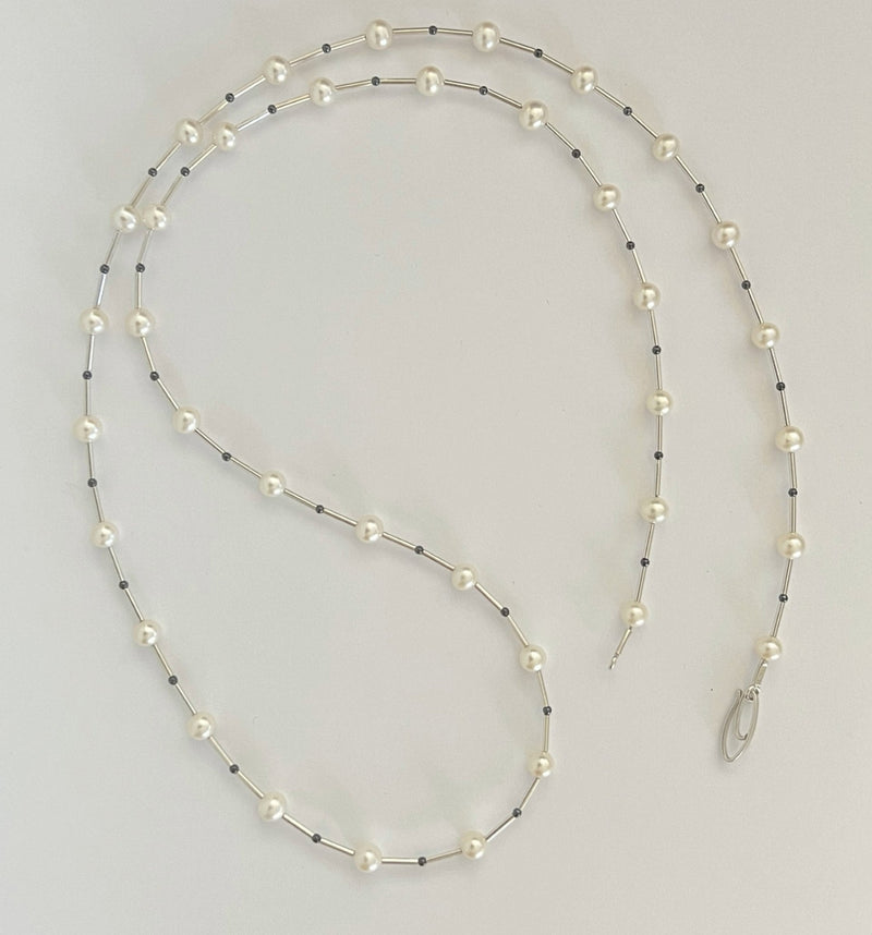 Long necklace with pearls and black beads on a light gray background