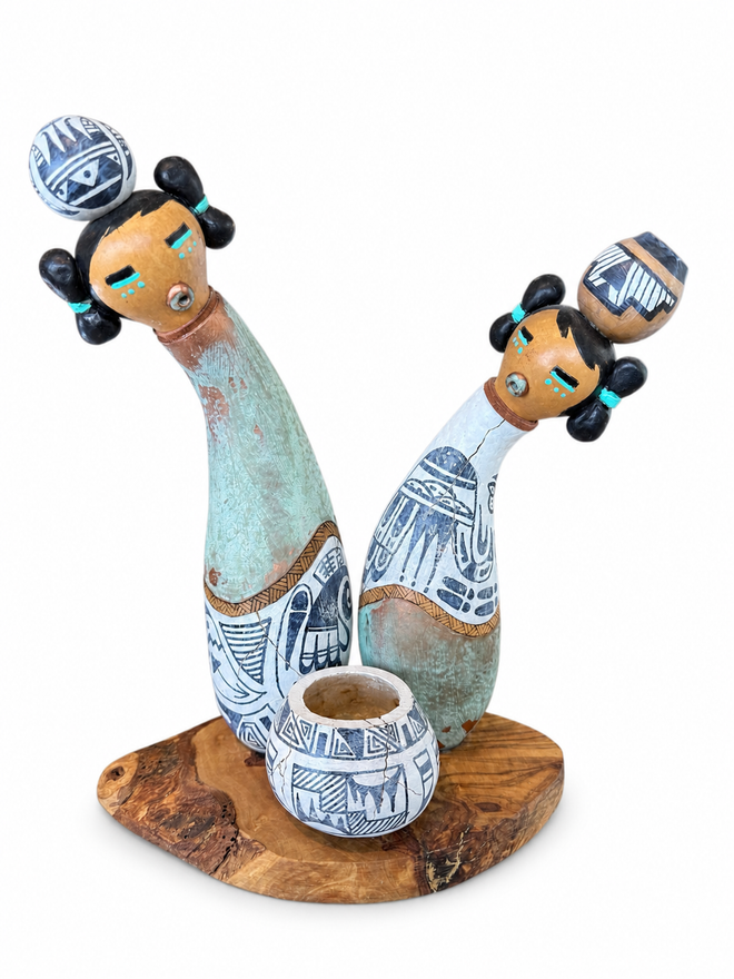 Handcrafted from natural gourds of varying sizes, this one-of-a-kind Two Maidens Kachina sculpture is a beautiful blend of Southwestern artistry and organic form. Each detail is individually hand-painted and enhanced with sculpted clay accents, rich copper patina, and touches of copper leaf, creating remarkable depth, texture, and character.