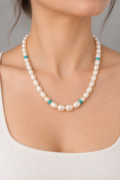 Woman wearing a 17-inch cream freshwater pearl necklace with Kingman turquoise bead accents, handmade by Lynnette Ammann in Sedona.
