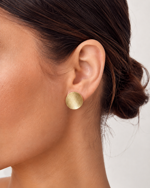 Gold curved disc stud earrings shown on ear