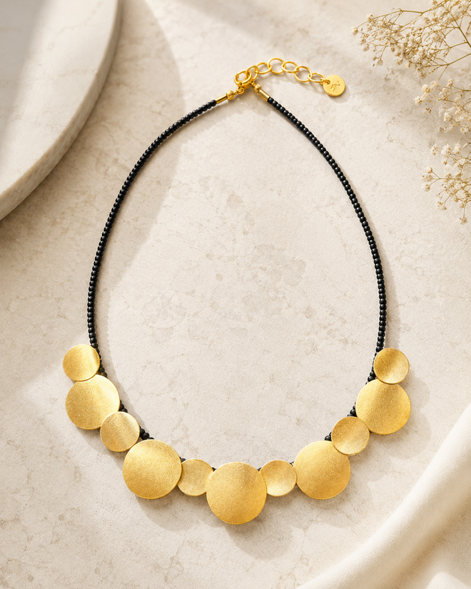 Gold plated statement disc necklace with black onyx beads on a neutral luxury background