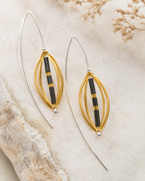 One-of-a-kind gold plated sterling silver earrings with hematite beads and long curved French hooks displayed on a natural stone background.