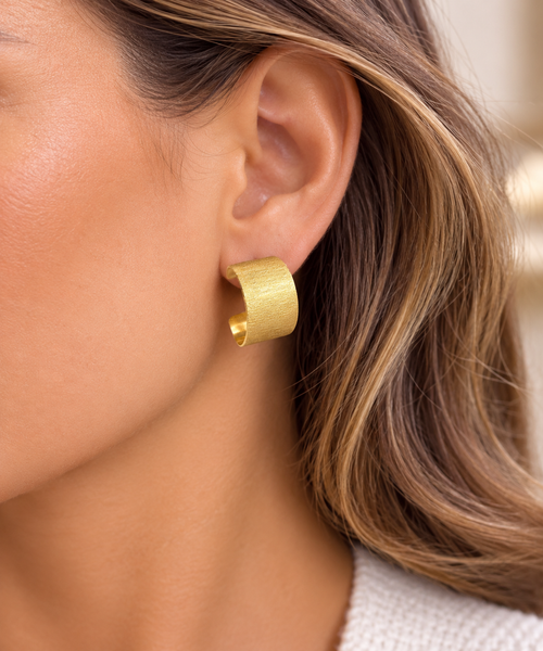 Model wearing matte gold vermeil wide hoop stud earrings with a brushed satin finish, handcrafted contemporary sterling silver jewelry for everyday elegance.