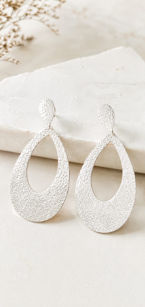 Close-up of handmade hammered sterling silver open drop earrings showing the artisan textured finish and lightweight craftsmanship.