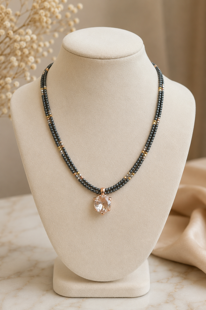 Handmade two-strand grey hematite necklace with a 12mm crystal pendant in a rose gold plated sterling silver setting displayed on a jewelry stand.