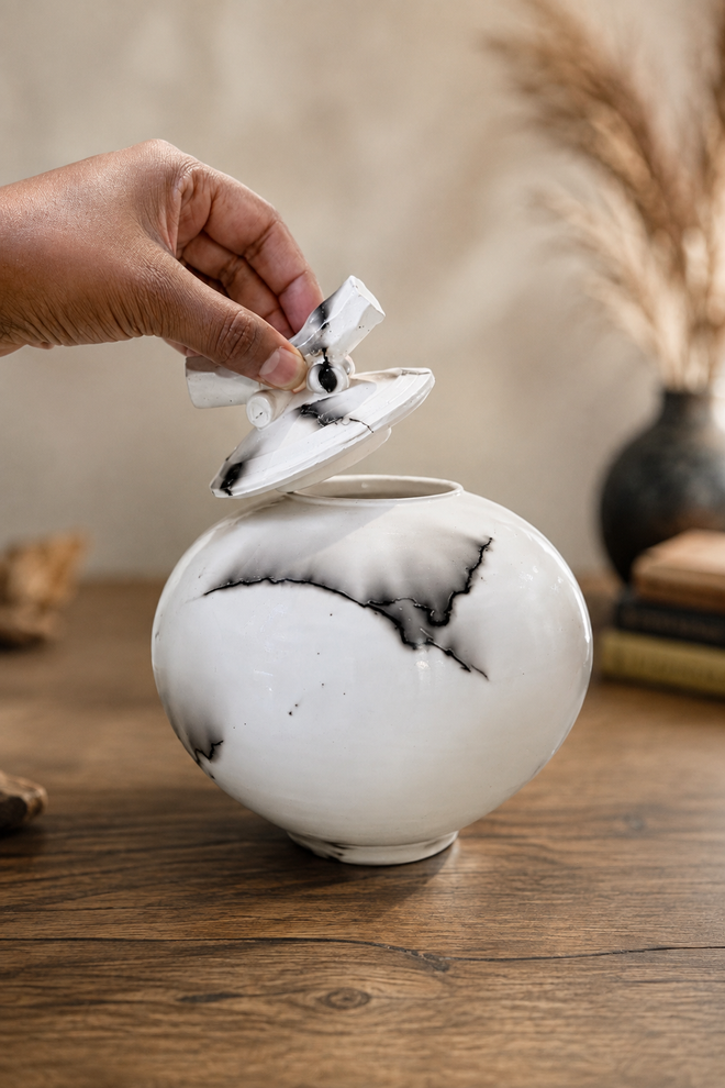 Hand lifting the decorative lid from a handmade horsehair pottery jar