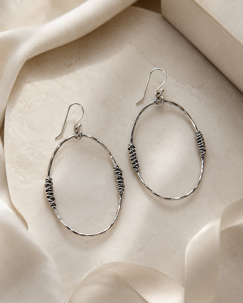 Large hammered silver open oval earrings styled in a luxury setting with soft neutral fabric