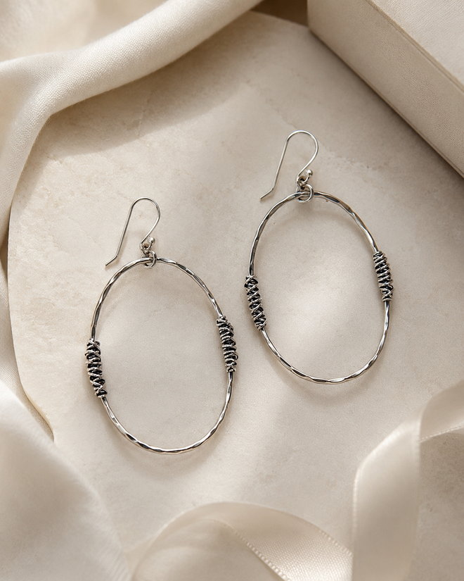 Large hammered silver open oval earrings styled in a luxury setting with soft neutral fabric