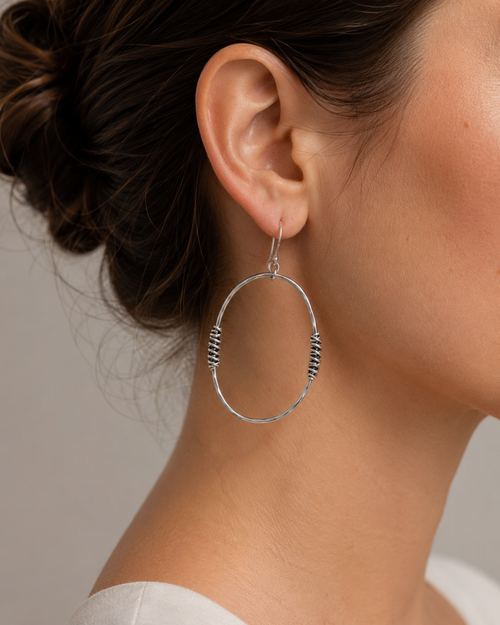Large hammered silver open oval earring worn on ear showing size and wrapped silver detail