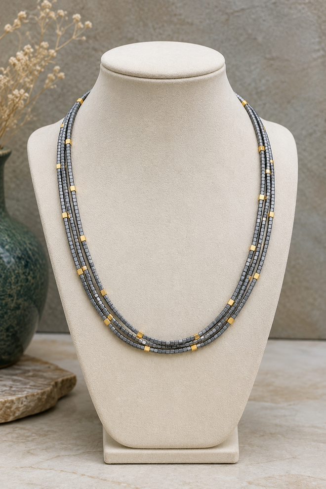 Elegant 4 strand light gray hematite necklace displayed on a jewelry bust featuring square cut hematite beads with 18K gold plated sterling silver accent beads.