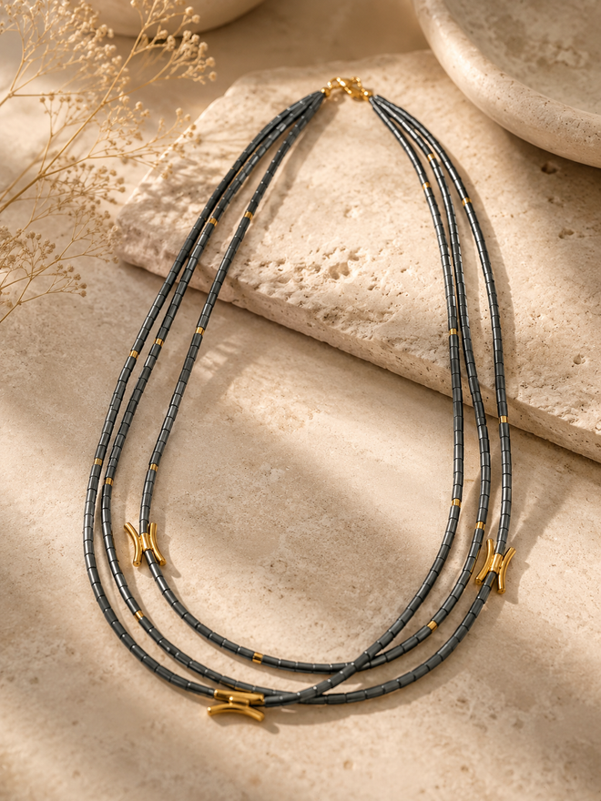 Luxury three-strand hematite necklace with gold accents displayed on elegant neutral stone background