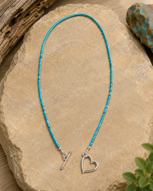Luxury product photo of Kingman turquoise bead necklace with sterling silver heart toggle clasp on cream display.