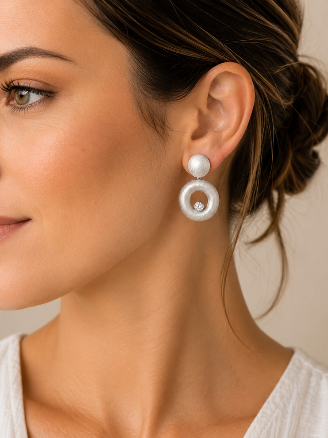 Model wearing handcrafted matte sterling silver convex circle drop earrings with sparkling white cubic zirconia, elegant contemporary designer jewelry for everyday luxury.