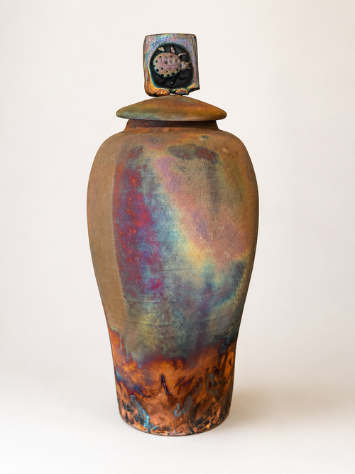 Tall handmade raku ceramic vessel with lid featuring an iridescent copper and earthy glaze