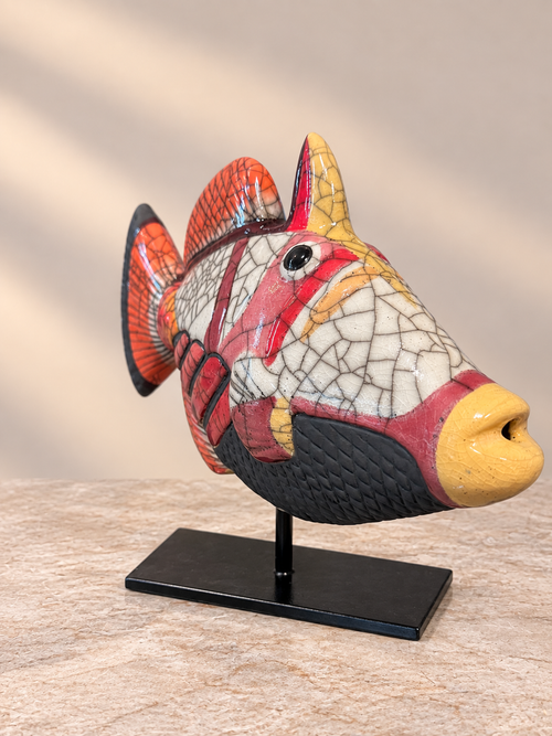 Angled view of one-of-a-kind coral red Raku pottery fish sculpture with detailed crackle glaze and black stand