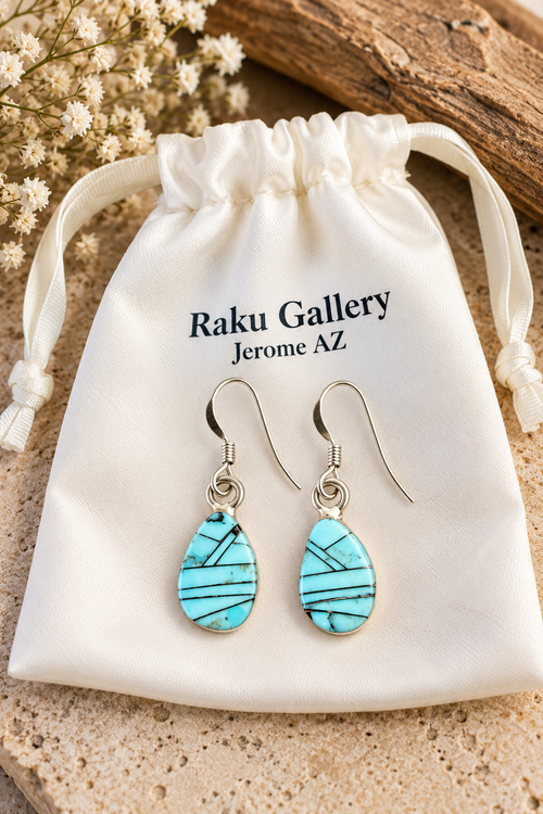 Sky-blue Golden Hills turquoise sterling silver earrings with geometric inlay displayed on a cream Raku Gallery jewelry pouch from Jerome, Arizona.