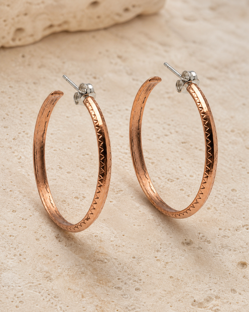 Close up of handmade Navajo copper half hoop earrings with stamped detail