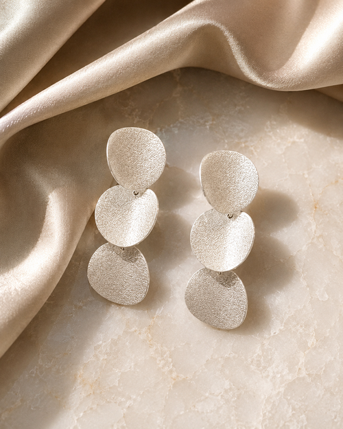 Textured sterling silver curved disc earrings in a luxury setting on marble