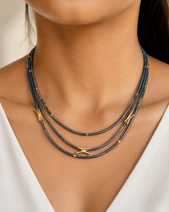 Three-strand hematite necklace with charcoal gray beads and gold accents on white background